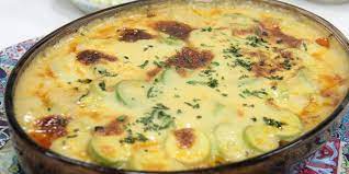 In a large saucepan over the fire, heat water mixed with a little salt, then add the zucchini to it after boiling, for 6 minutes. Transfer the drained zucchini to an ice bath to stop cooking, then remove and drain well. In another saucepan, heat the oil, then fry the onions until soft. Add the meat and stir well, until it turns brown. Add the spices and mix well, then remove the pot from the heat. Mix the milk and béchamel powder in a separate saucepan over the heat, and cook, stirring, until it boils. Keep stirring after boiling until the consistency of the sauce. Pour a little bechamel sauce at the bottom of an oven tray, then spread half the amount of zucchini over it. Add the minced meat over the zucchini and distribute it evenly, then arrange the tomato slices on top. Evenly distribute the rest of the zucchini on top, then cover with the remaining béchamel sauce. Spread grated Parmesan cheese on top, then put the tray in the oven preheated to 200°C, for 30 minutes